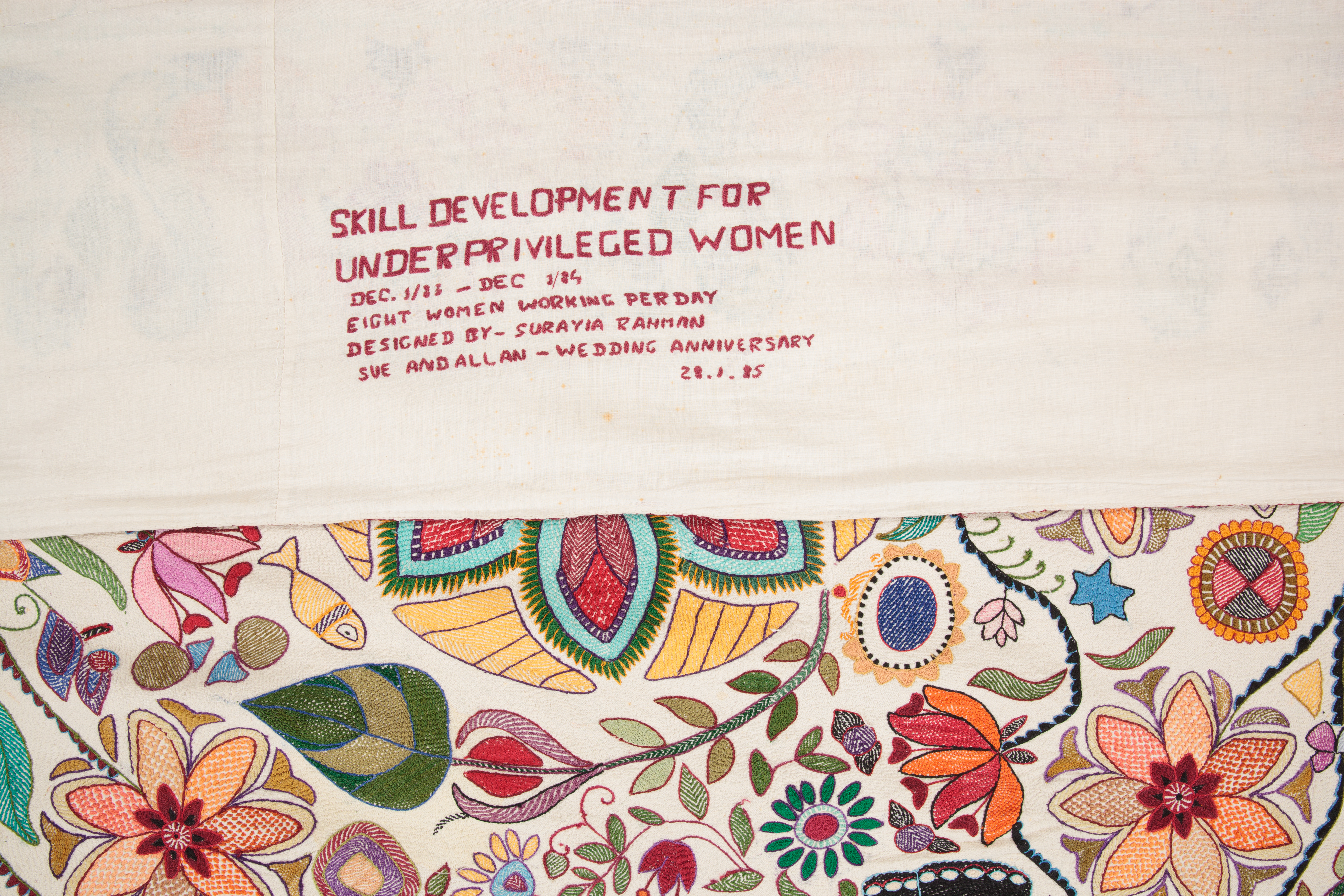 Close up of the production and provenance information embroidered on the reverse. Text says 'Skill Development for Underprivileged Women. DEc 1983 - Dec 1984. Eight women working per day. Designed by Surayia Rahman. Sue and Allan - Wedding Anniversary. 28.1.85'